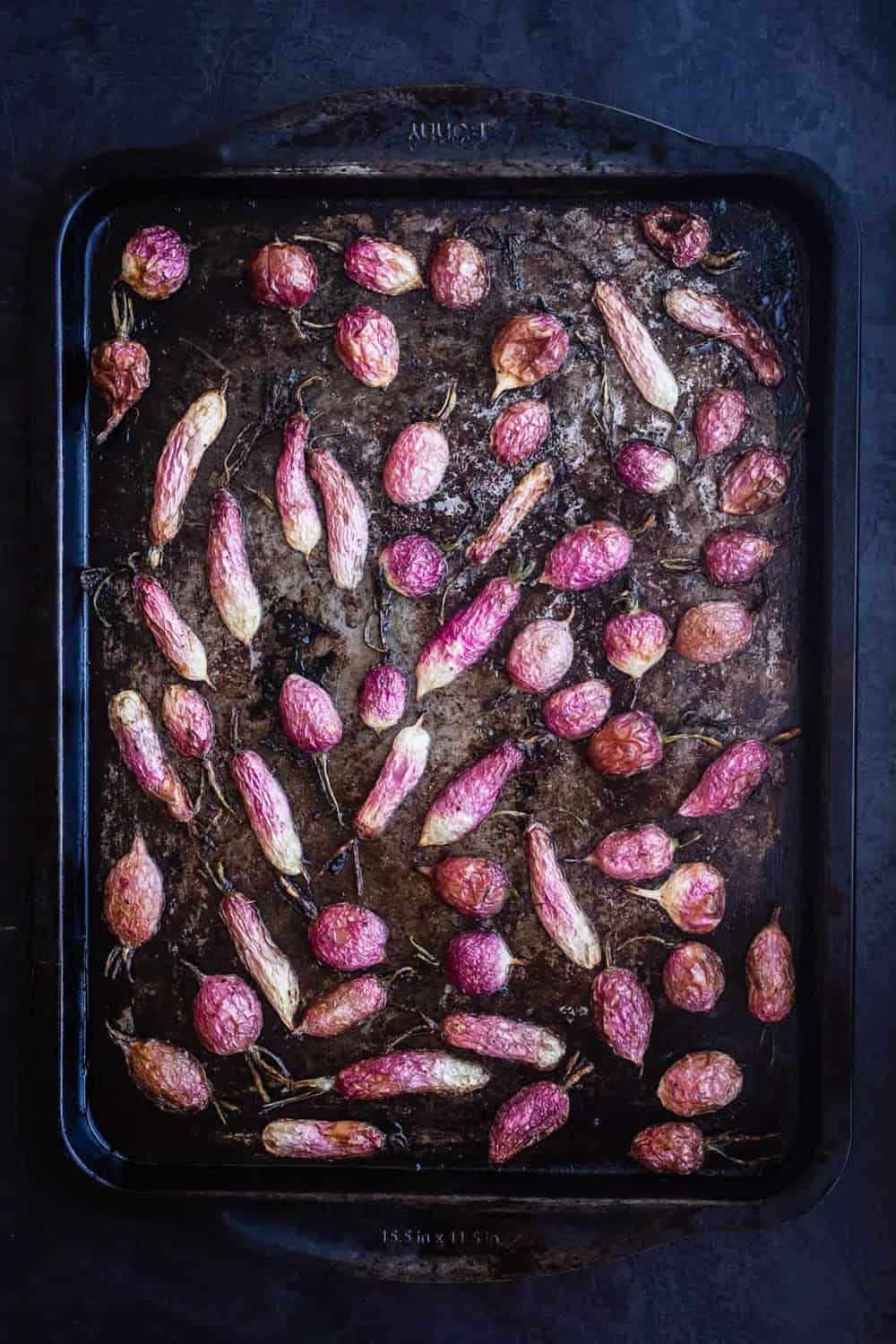 Roasted radishes just out of the oven, on a baking sheet on a black background.
