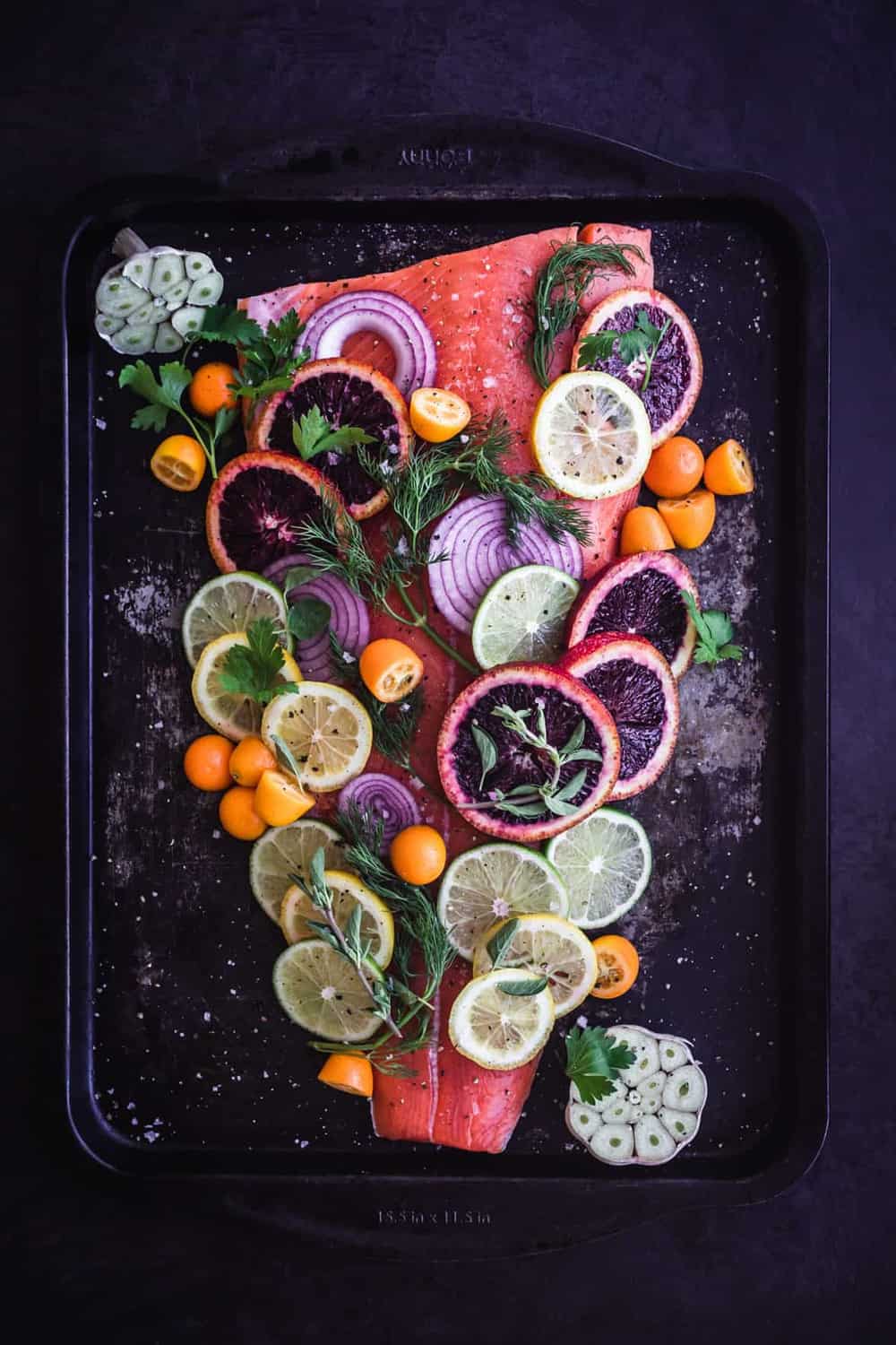 Citrus & Fresh Herb Roasted Salmon. Pre Oven with blood oranges, lemons, Meyer lemons, limes, kumquats, red onions, garlic, parsley, and dill on the salmon.