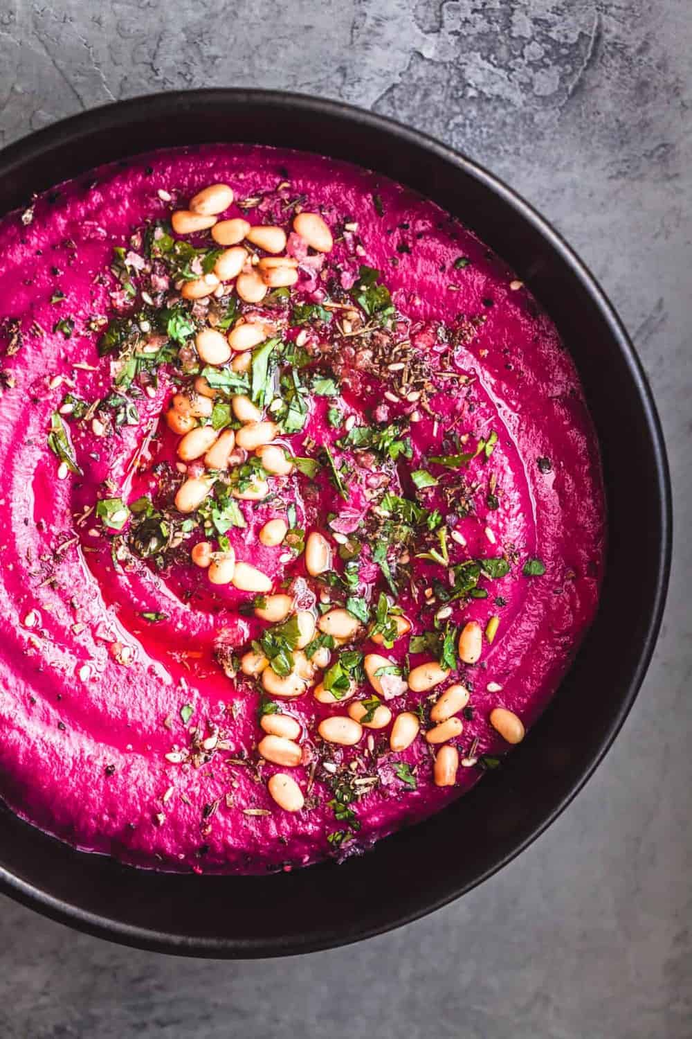 Roasted Beet Hummus with Pine Nuts, Parsley, Za'atar in a black bowl.
