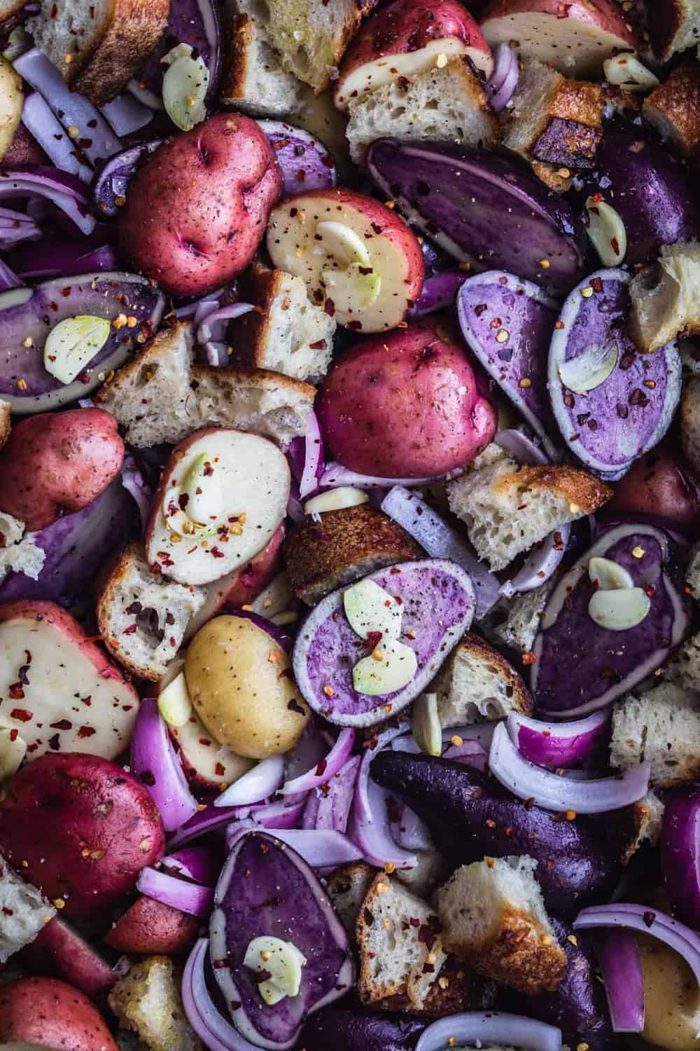 The potatoes and bread cubes cut up with garlic slices, red onion, and chili flakes.