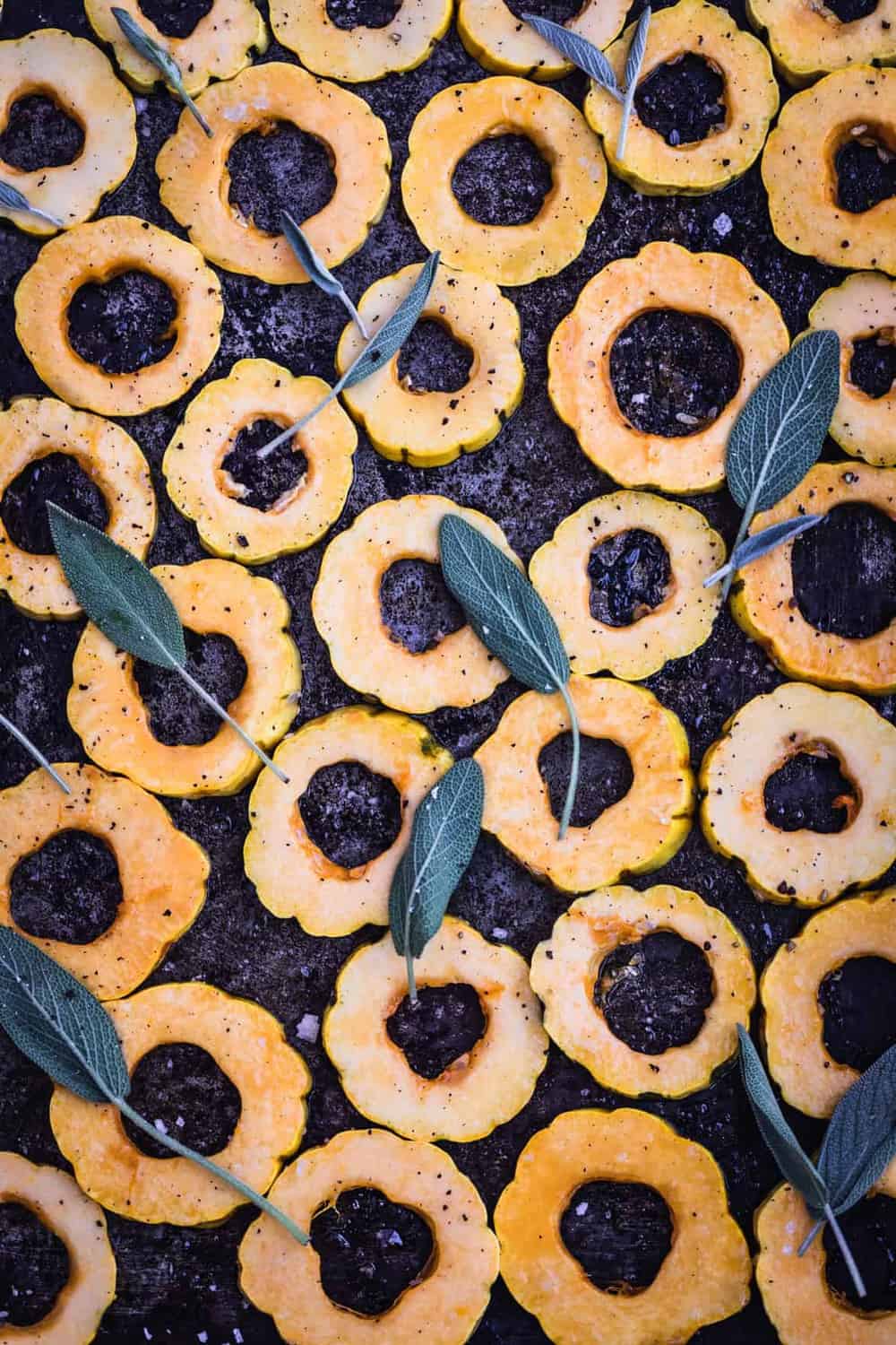 Sliced roasted squash rings on baking sheet, up close, topped with fresh sage leaves. Pre Oven.