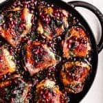 Pomegranate Chicken topped with pomegranate arils and parsley, in cast iron skillet on a white background; overhead shot.