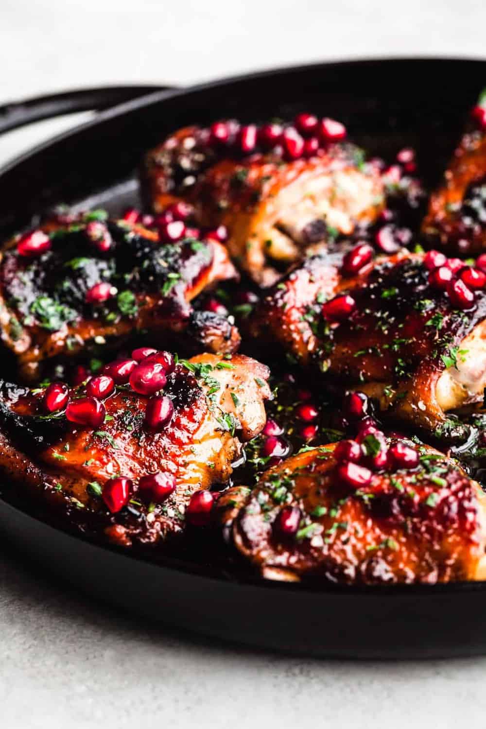 Pomegranate Chicken, out of the oven and all done, in a cast iron skillet on white background. Side angle shot with the right side cut off.