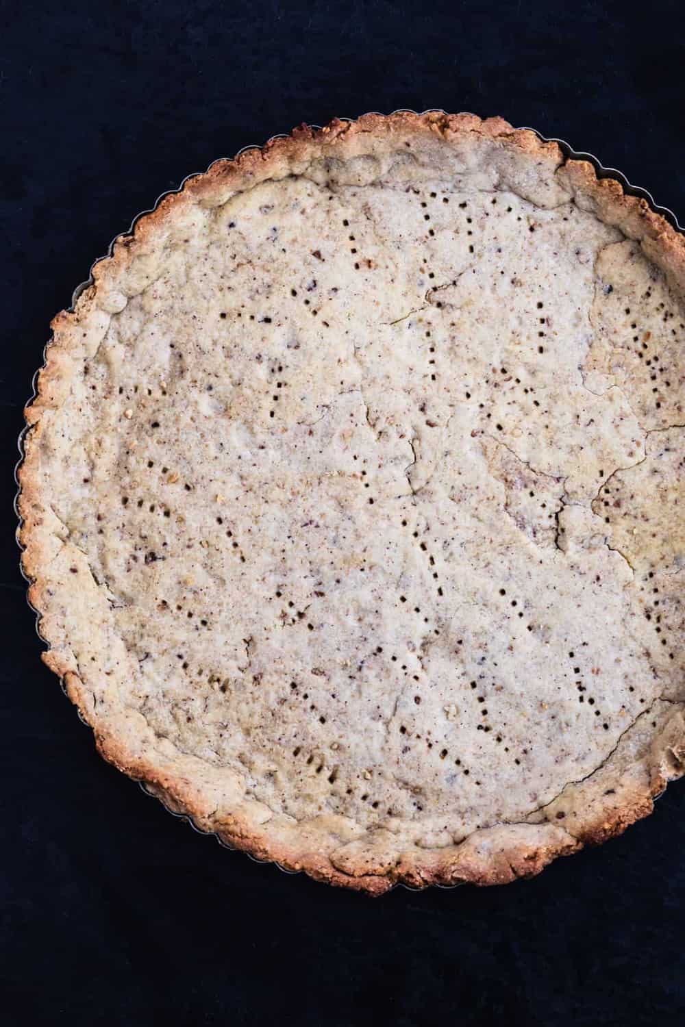 Par baked tart crust, in a tart pan, on a black background.