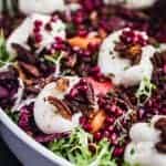 Burrata on top of frisee and radicchio with pears, persimmons, pomegranate and pecans scattered on top a serving plate.