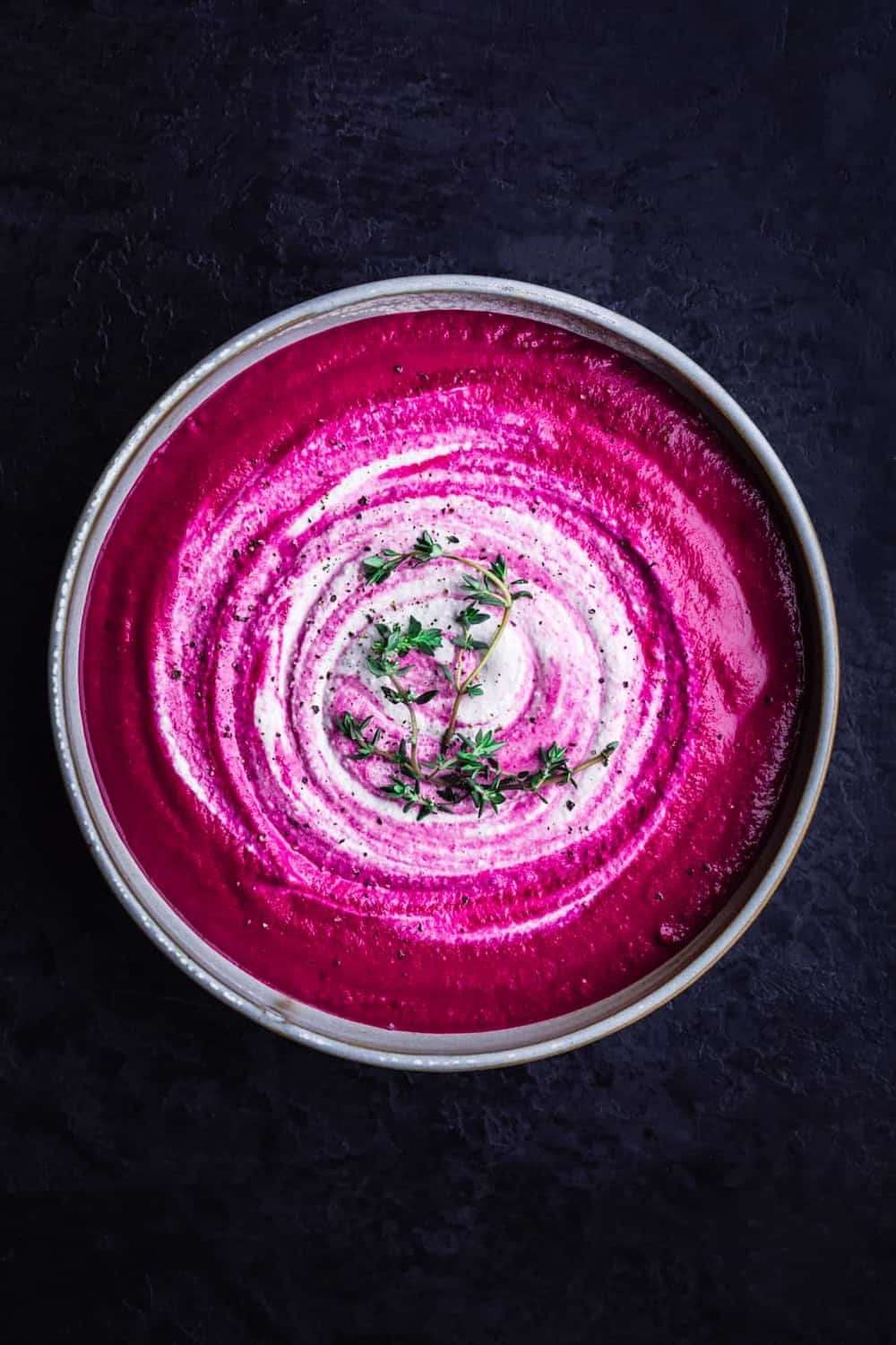Roasted beet soup with cashew cream swirl. Overhead shot, black background.
