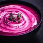 Roasted Beet Soup with Cashew Cream swirl and thyme sprigs, side angle shot on a black background.