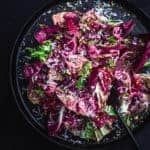 Blood Orange and fennel salad with chicories, pistachios, shredded cheese, mint and shallots on a black plate with a fork.
