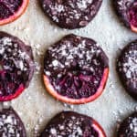 Candied Blood Oranges dipped in Chocolate with Flaky Sea Salt on parchment paper.