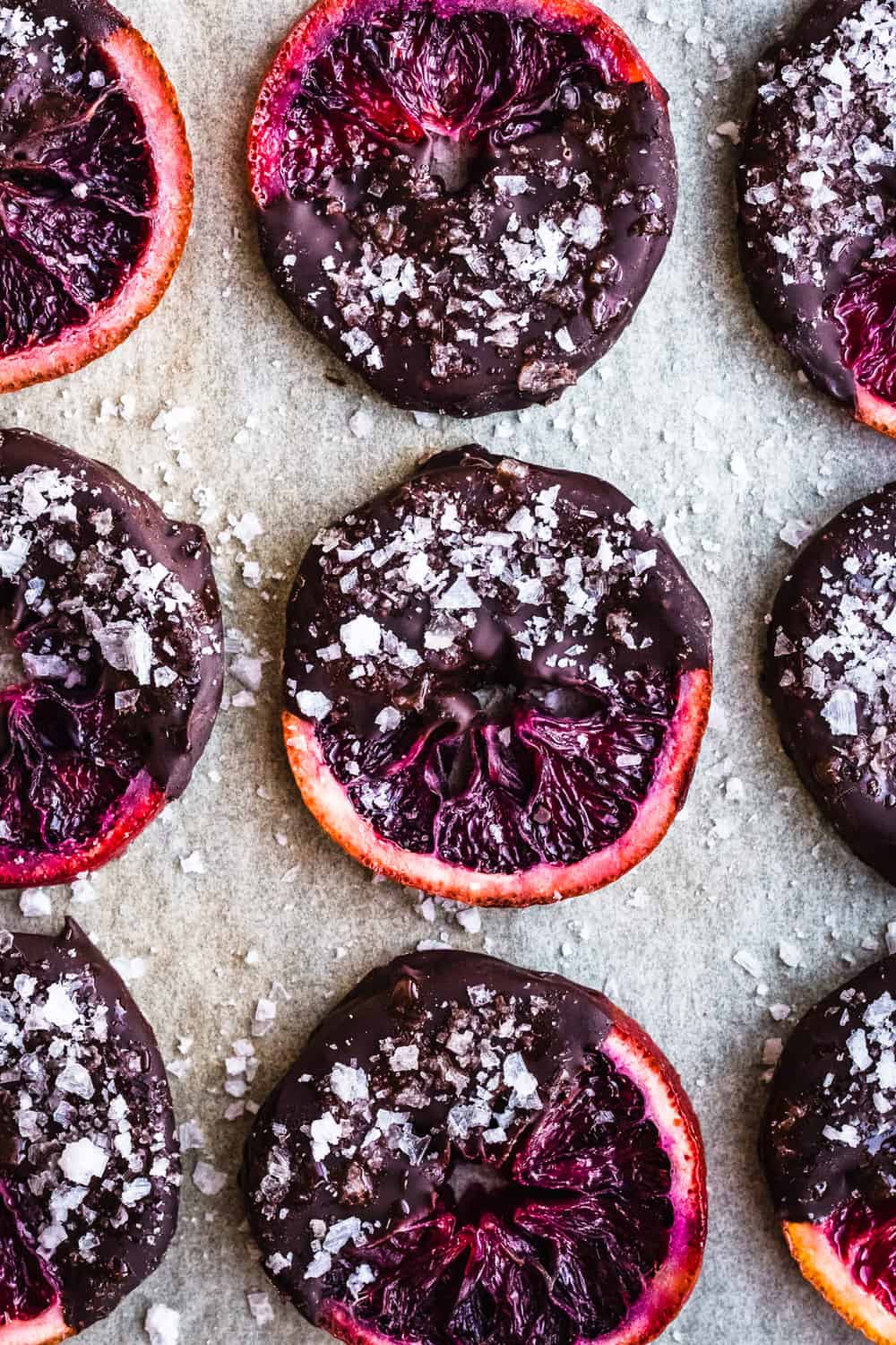 Candied Blood Oranges dipped in Chocolate with Flaky Sea Salt on parchment paper.