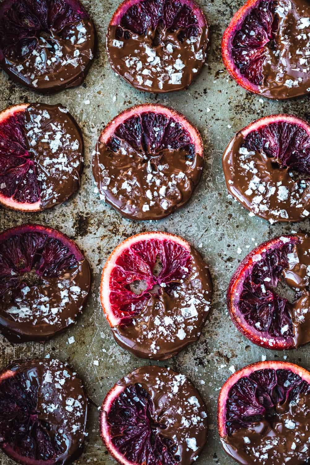 Candied Blood Oranges dipped in Chocolate with Flaky Sea Salt on a pan.