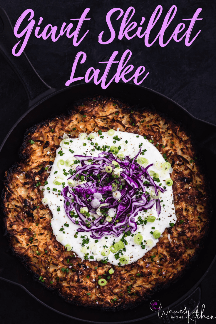 Giant potato latke in pan with sour cream, purple cabbage, scallions and chives.
