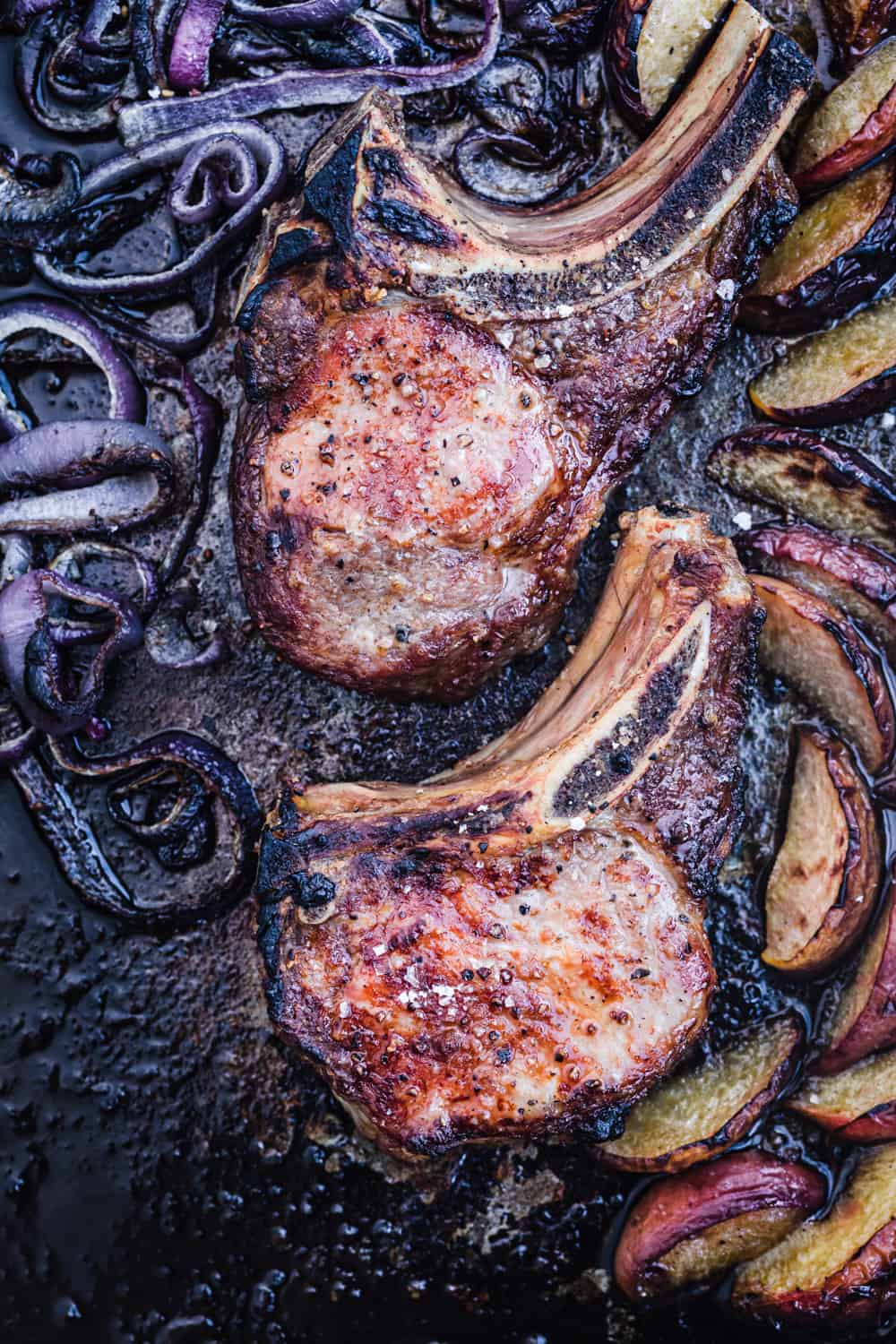 Sheet pan with bone-in pork chops, peaches and onions just out of the oven, overhead shot.