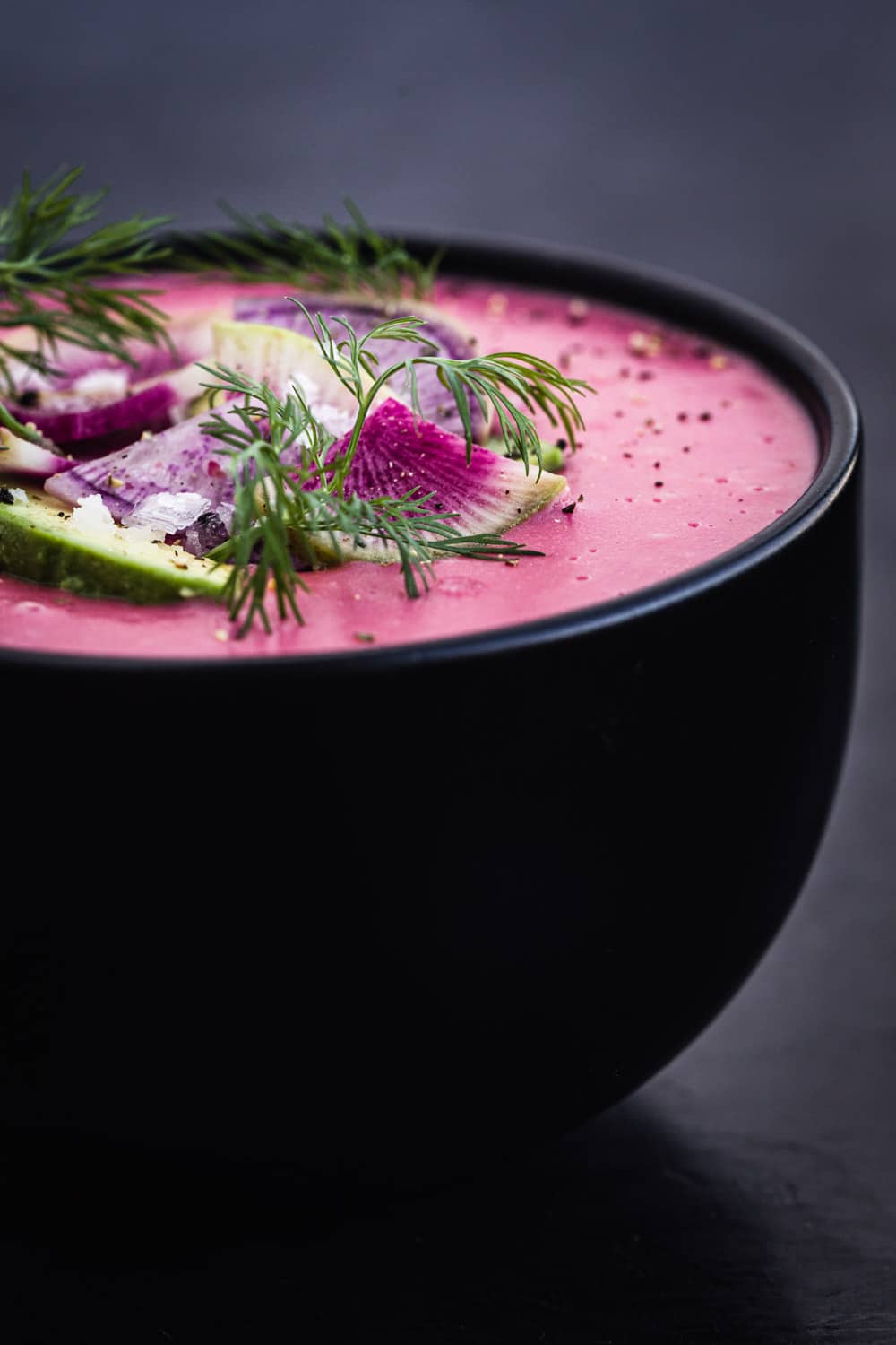 side angle shot of pink vegan potato soup with radish, avocado and dill topping.
