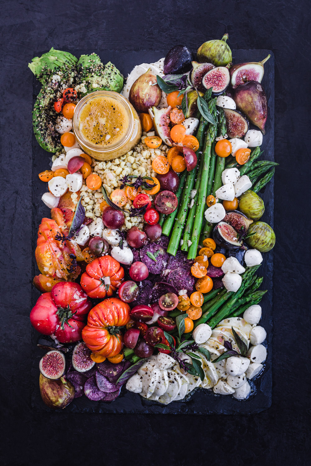 Summer salad board filled with seasonal summer fruit and veggies, overhead shot on a black background.