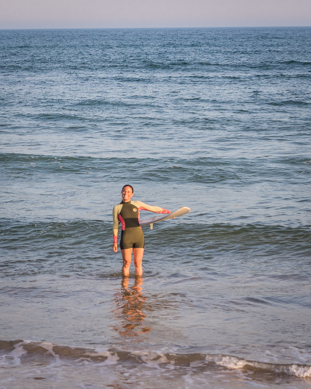Chef Daniela Gerson in a wetsuit in the ocean with her surfboard in Ditch Plains, NY.