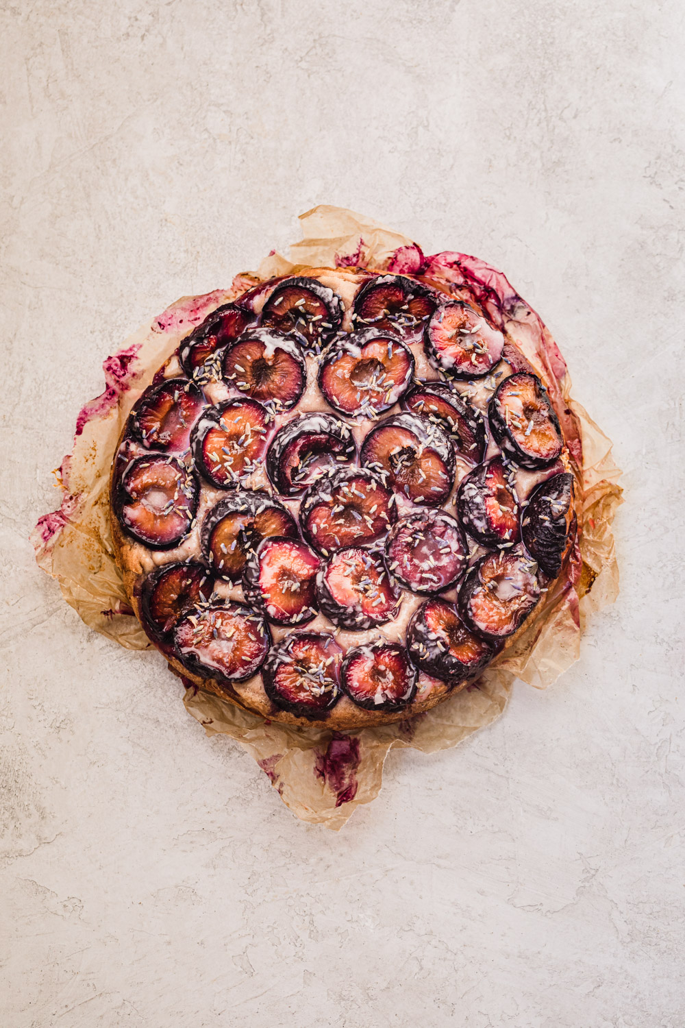 Overhead shot of the plum, walnut and lavender cake on parchment paper, on a white background.