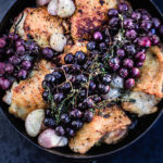 Close up shot of the finished thyme roasted chicken with shallots and grapes, in a cast iron skillet.