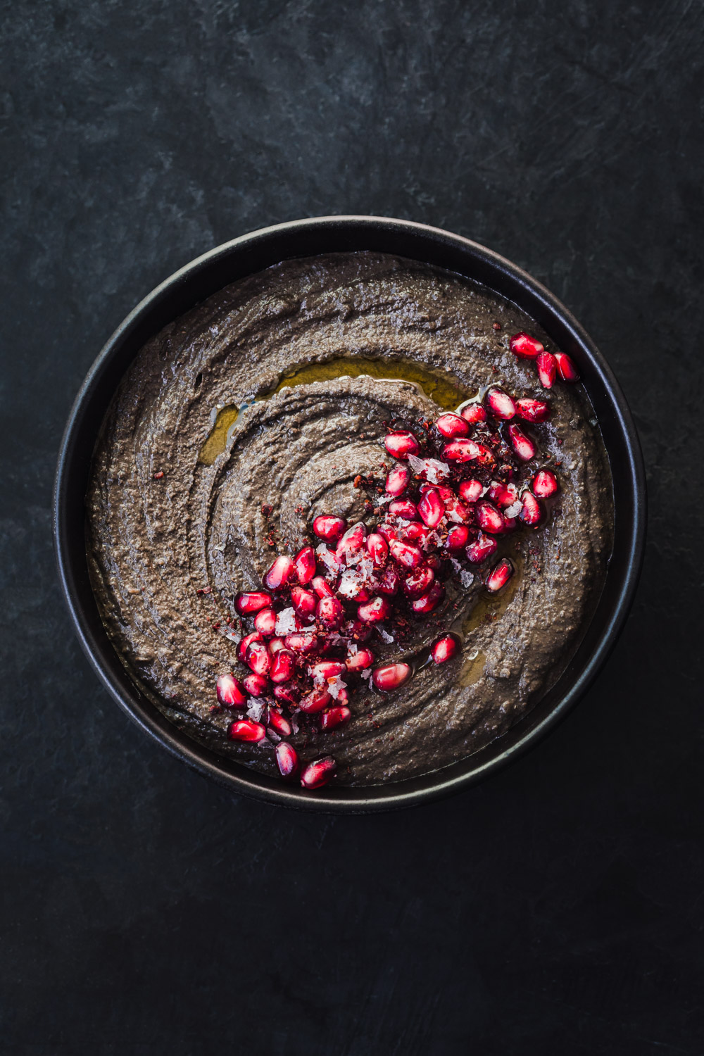 bowl of black hummus, overhead shot, bowl is centered in frame on a black background