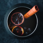spiced wine poured into a black mug with a cinnamon stick, star anise, cloves, and sliced citrus.