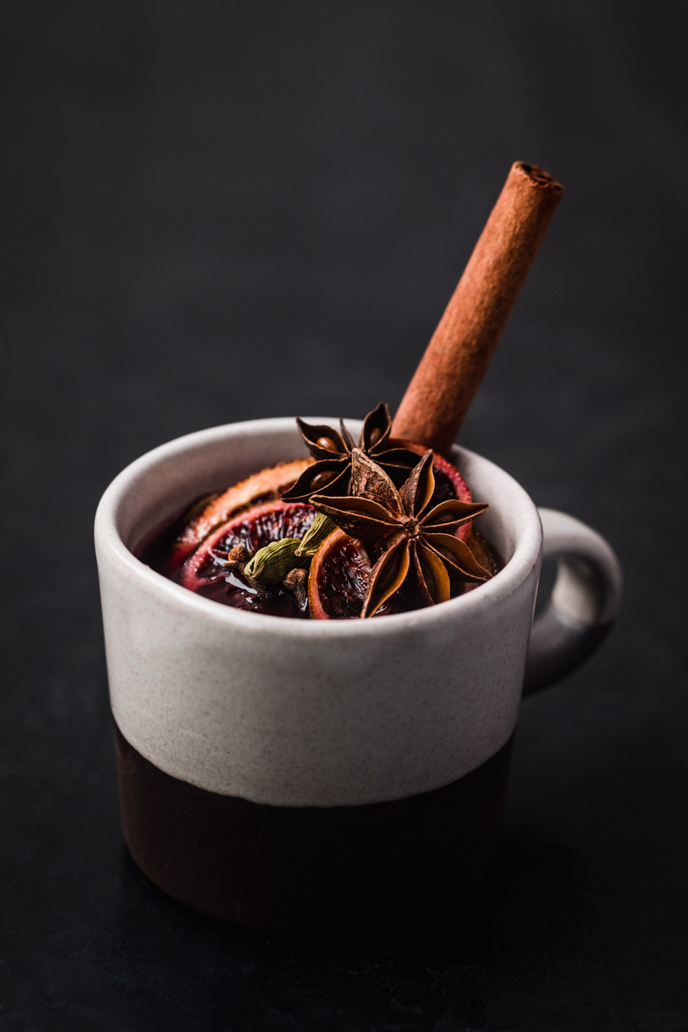 Side angle shot of spiced wine with a few star anise, cardamom pods, blood orange and cloves.