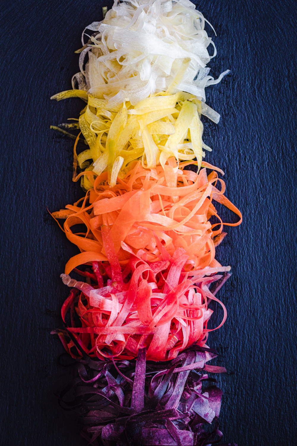 in process shot of piles of colorful carrot ribbons shaved, white, yellow, orange, coral and purple