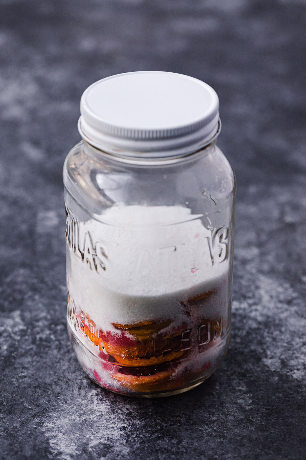 Thin blood orange slices in a mason jar covered with salt and sugar