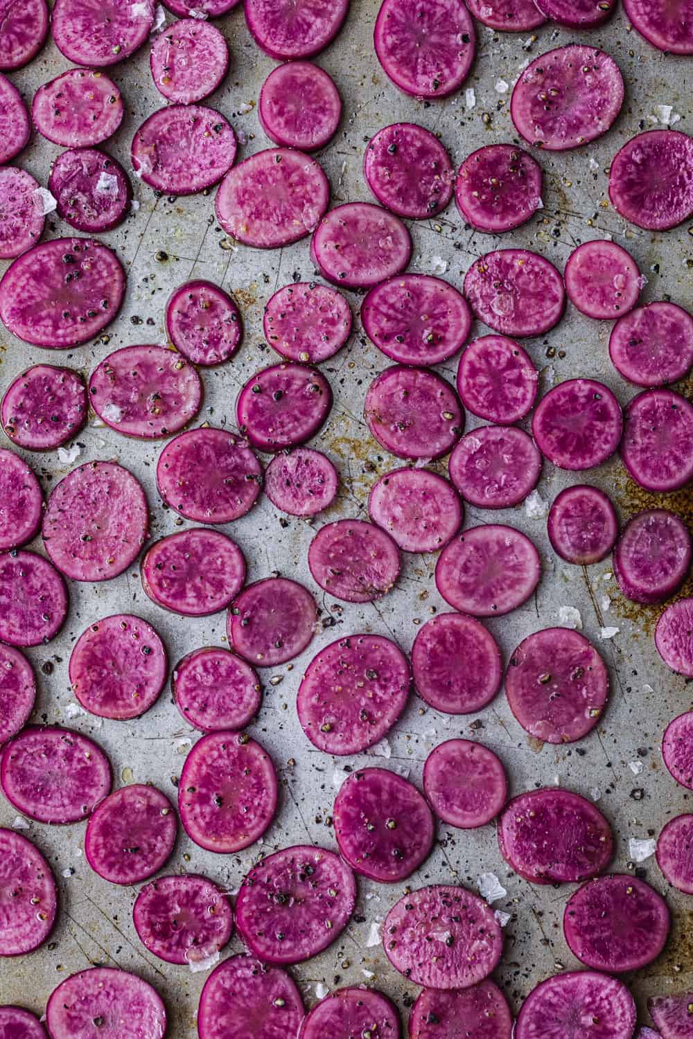 up close shot of pink potatoes thinly sliced on a cookie sheet with olive oil, salt and pepper to be used in the farmers market salad