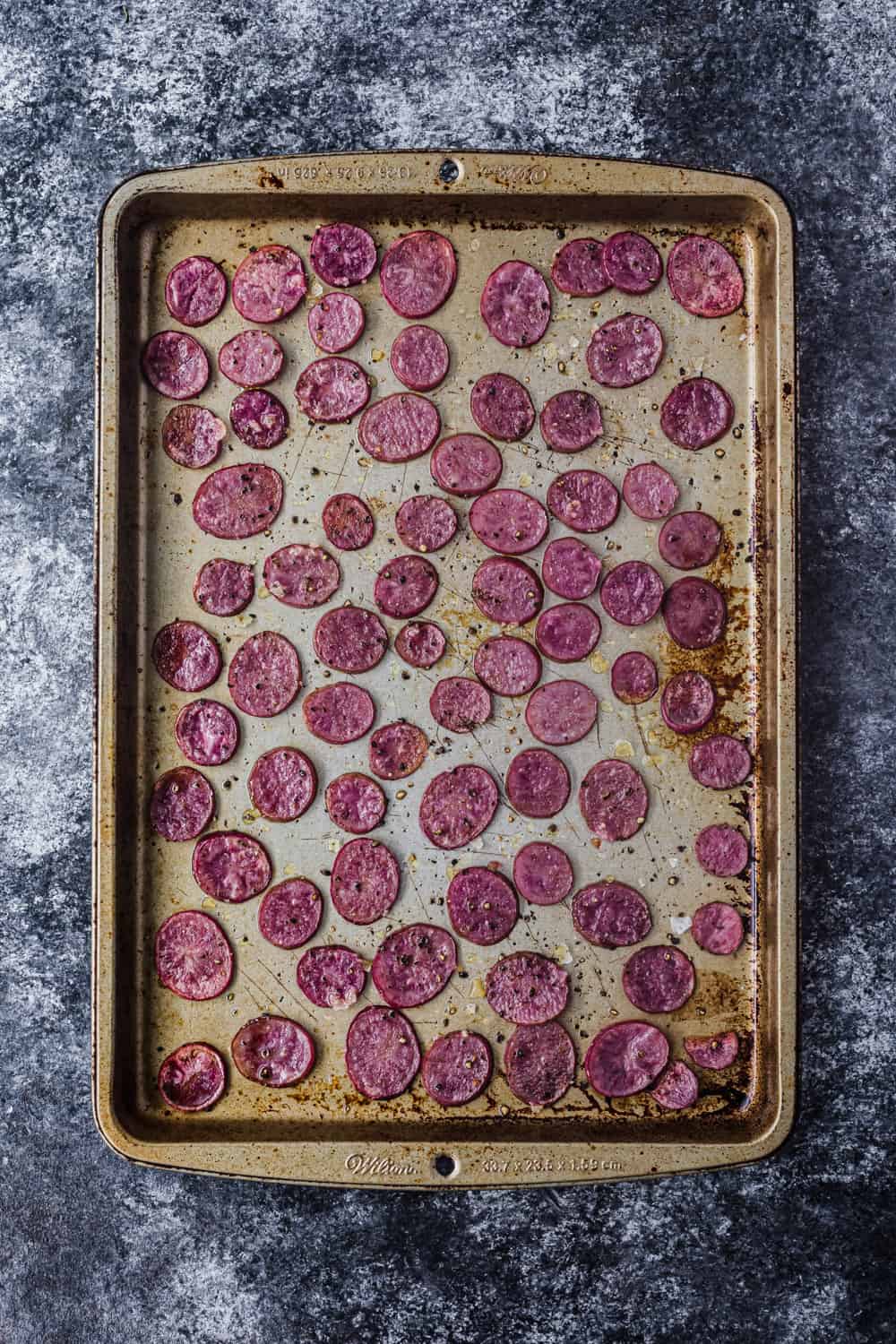Overhead shot of a baking sheet with thinly sliced roasted pink potatoes, to be used in the farmers market salad