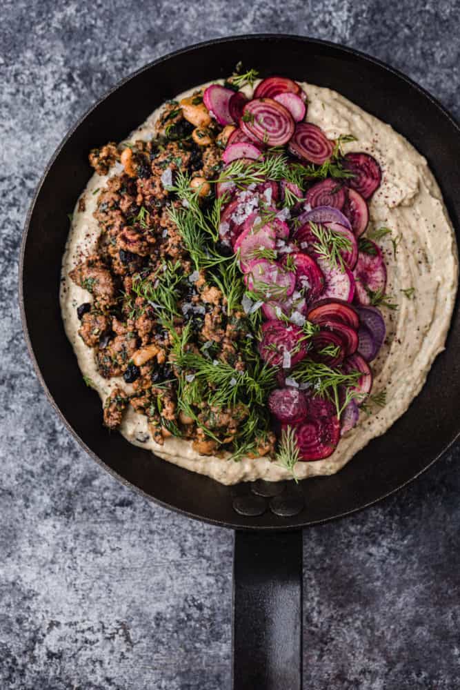 overhead shot of hummus topped with warm spiced lamb, dill, pine nuts and currants.