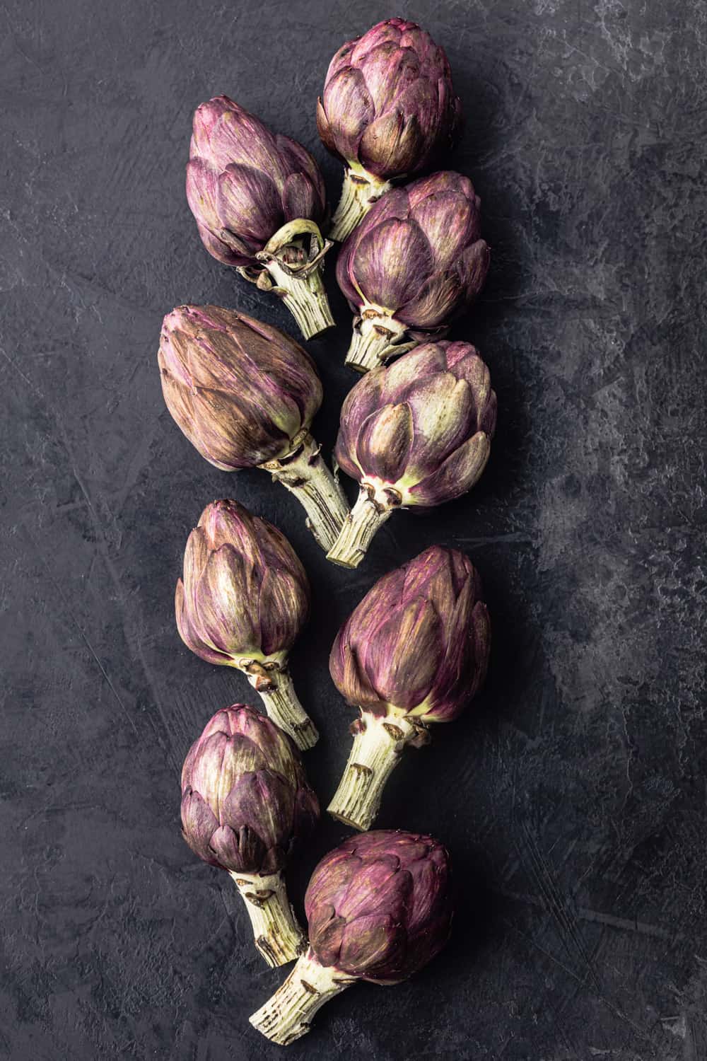 9 whole baby artichokes, raw and on a black background.