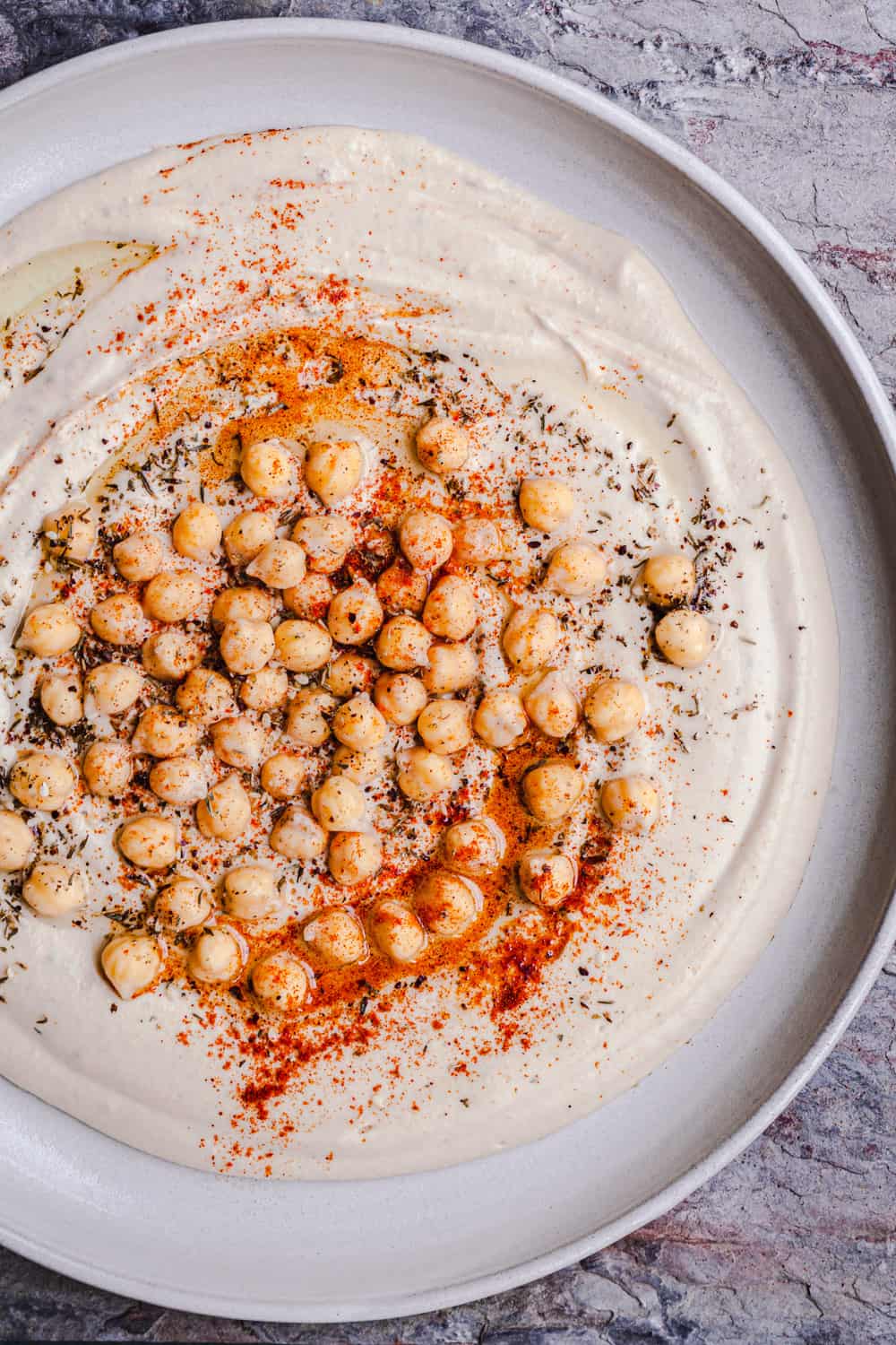 smooth and creamy hummus on a plate topped with chickpeas, spices and olive oil, overhead shot