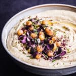 side angle shot of creamy hummus with tahini in a bowl on a dark background