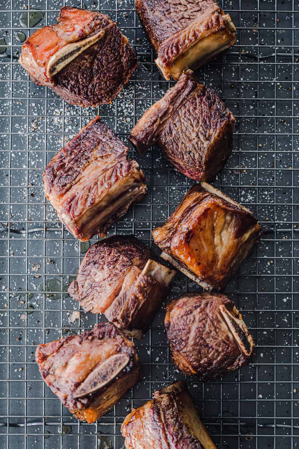In process shot, short ribs seared on all sides, on a wire rack on a baking tray.
