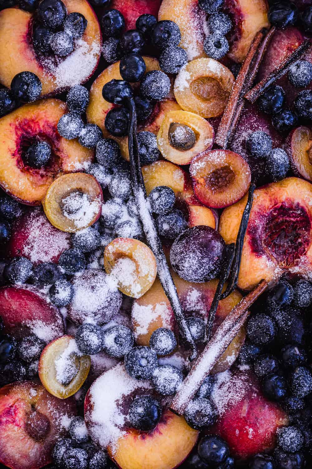 raw stone fruit with blueberries, vanilla beans, cinnamon and sugar on a baking sheet and all ready to go in the oven and be cooked.