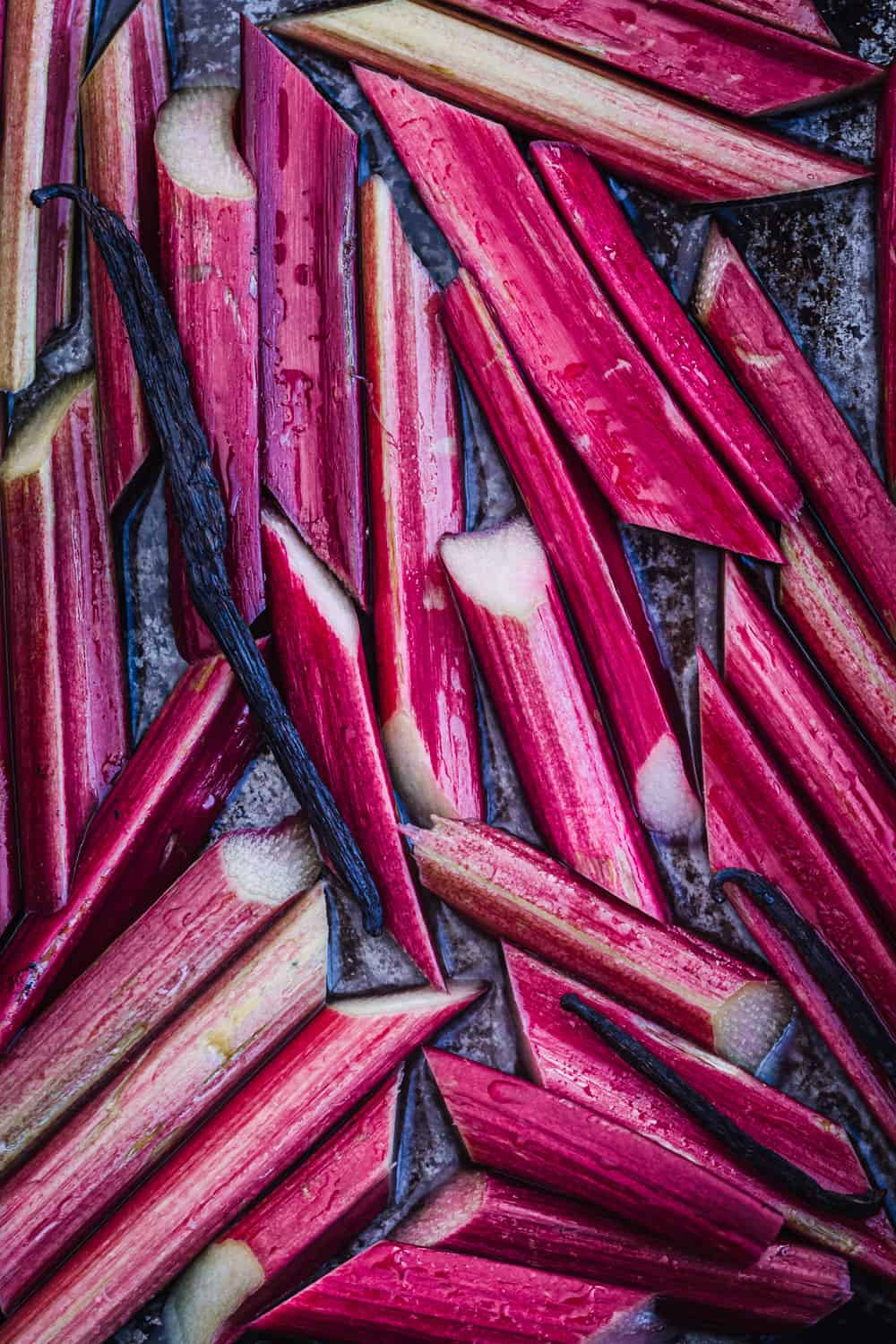 Raw rhubarb stalks sliced on a tray with vanilla and ready to be cooked in the oven.