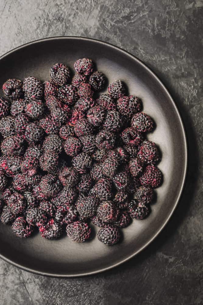 a black plate filled with deep-purple/black raspberries, overhead shot.