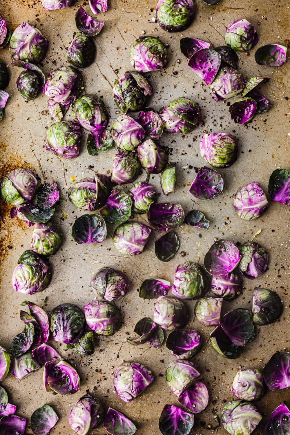 In process shot of raw Purple Brussels sprouts cut in half, tossed with olive oil, salt and pepper; overhead and pre-oven shot.