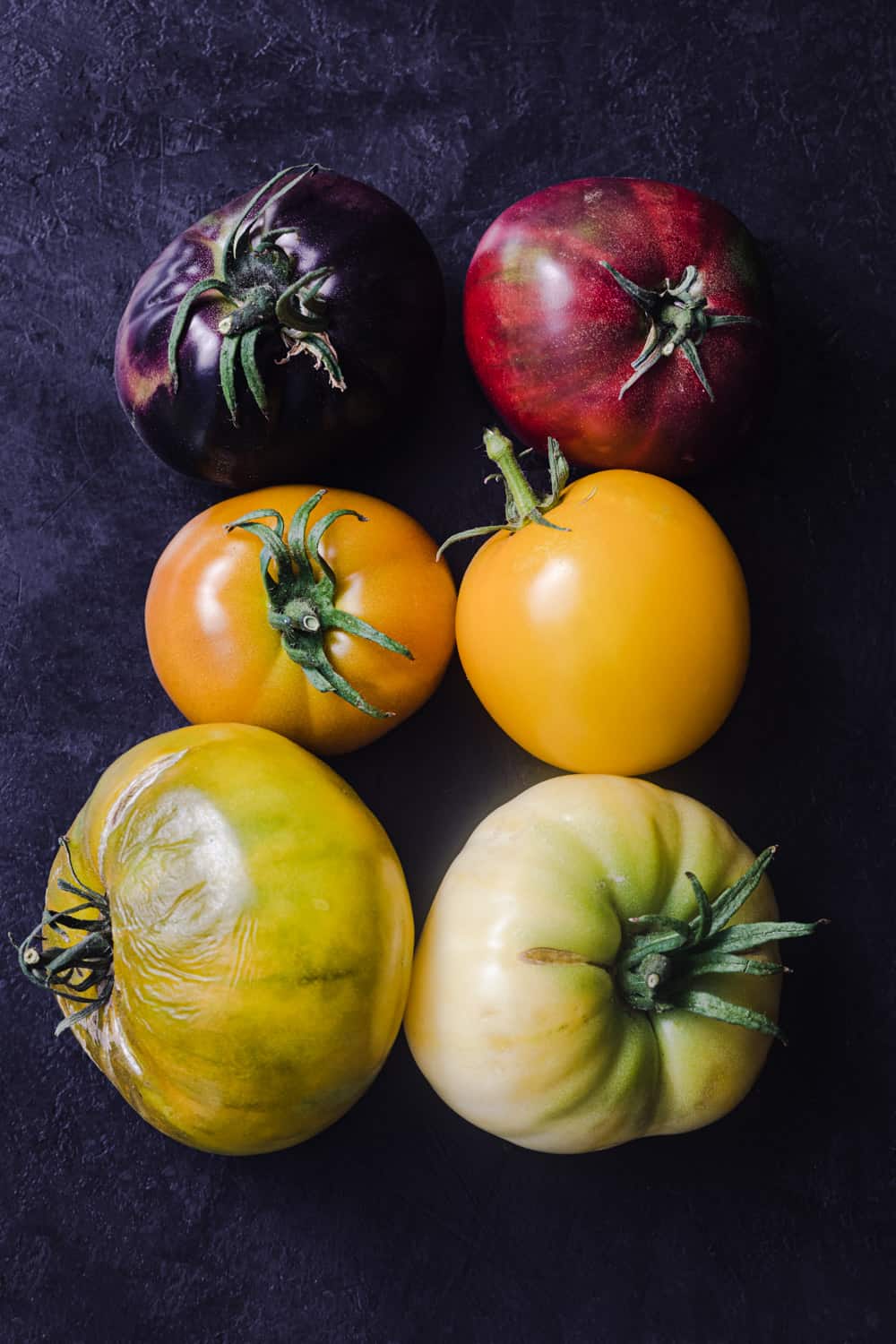 A tomato rainbow! 6 heirloom tomatoes in different colors: Deep purple, deep red, orange, yellow, yellow-green and green-white.