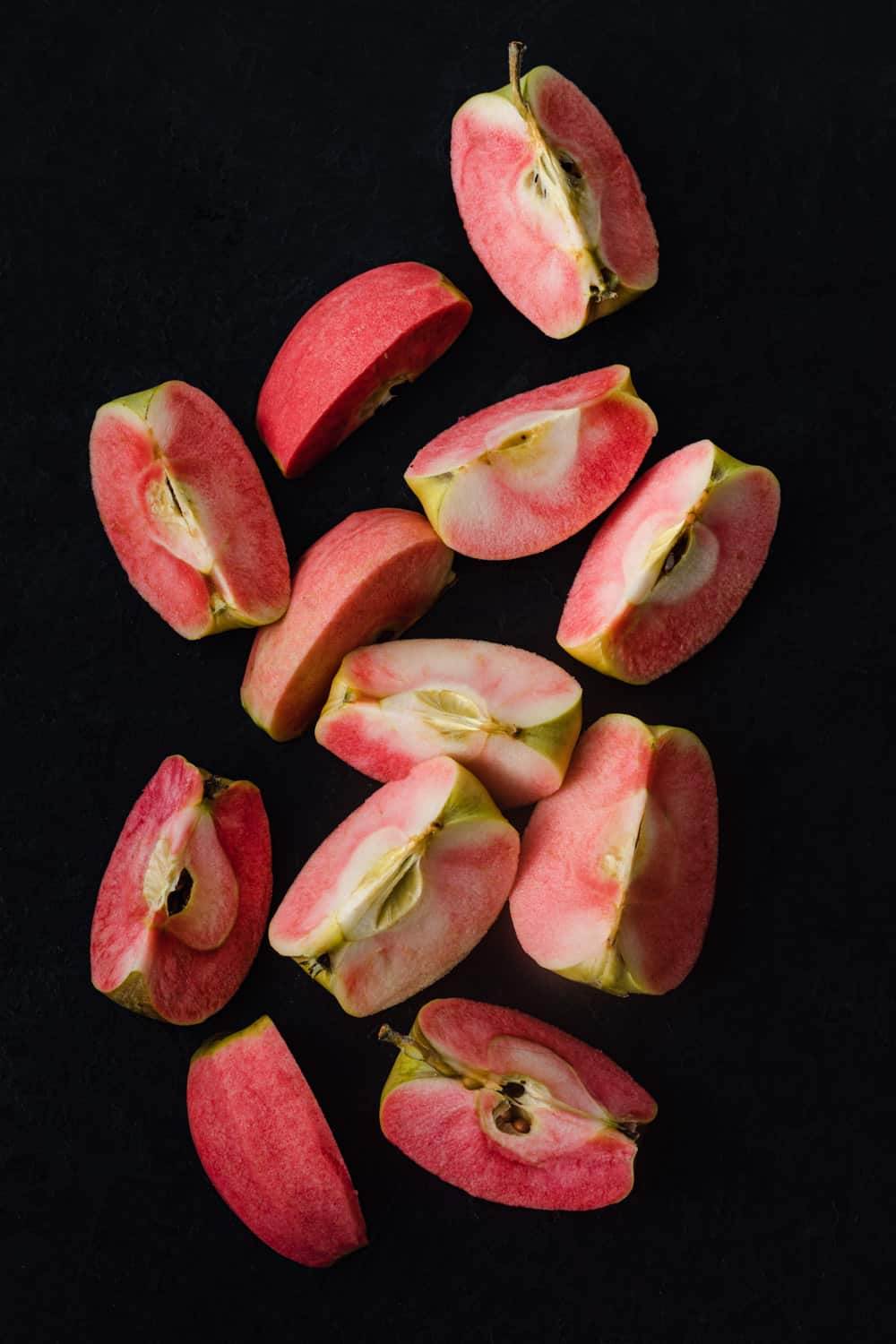 Pink Hidden Rose apples, cut into quarters, on a black background; overhead shot.