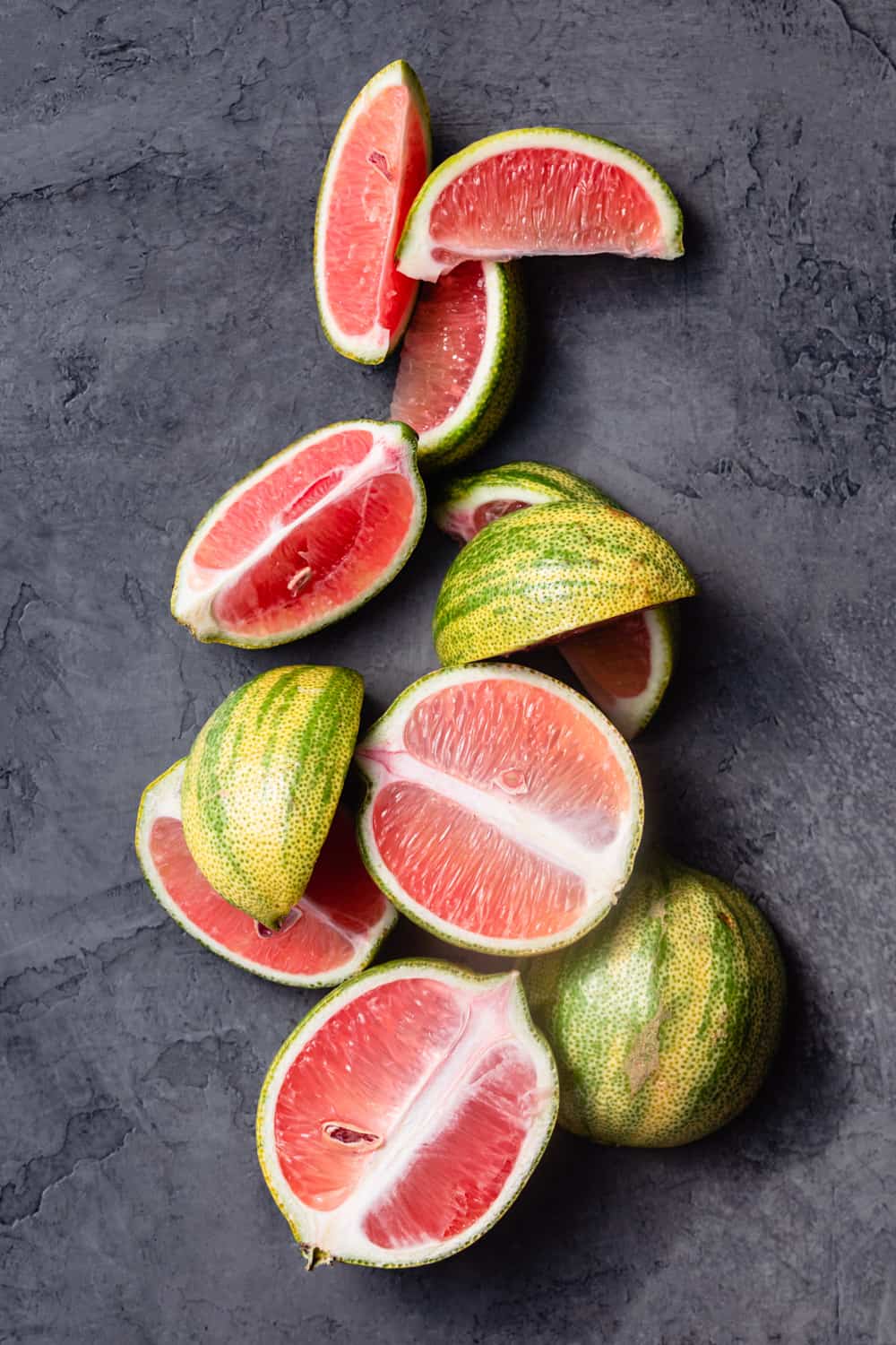 Pink lemons cut open, some in half and some in quarters, arranged artistically on a grey background; overhead shot.