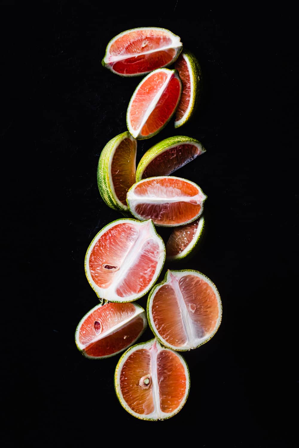 pink fleshed lemons with variegated green and yellow striped rind outside cut into wedges on a black background; overhead shot.