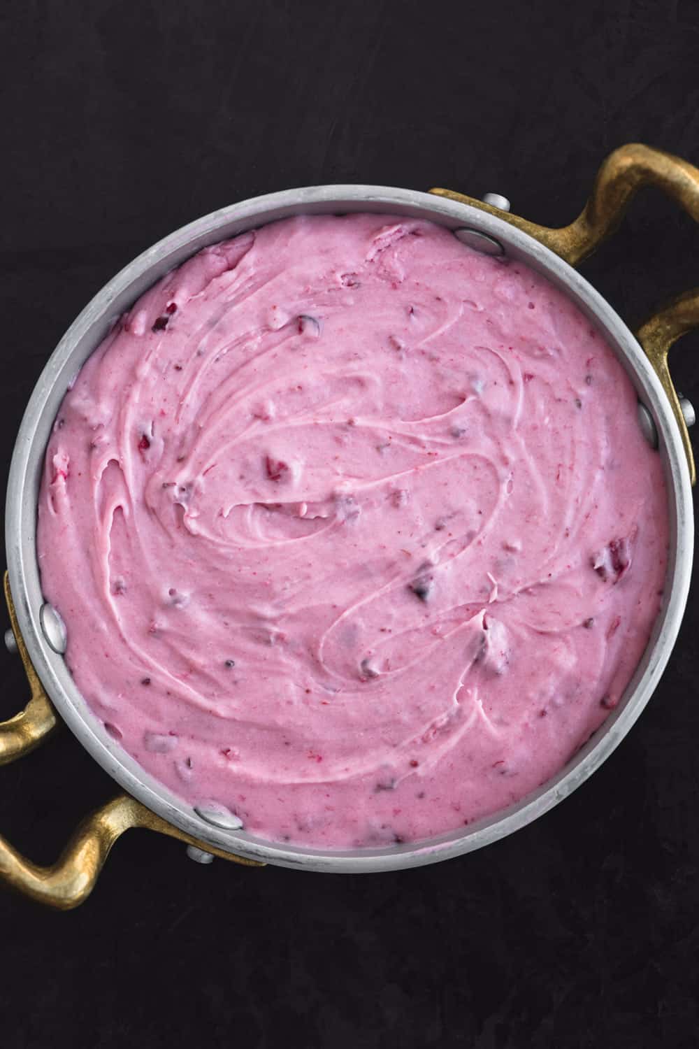 Freshly made cranberry cream cheese frosting in a silver bowl with gold handles, overhead shot on a black background.