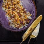 Purple sweet potato pie on a black baking sheet with gold serving utensils, overhead shot.
