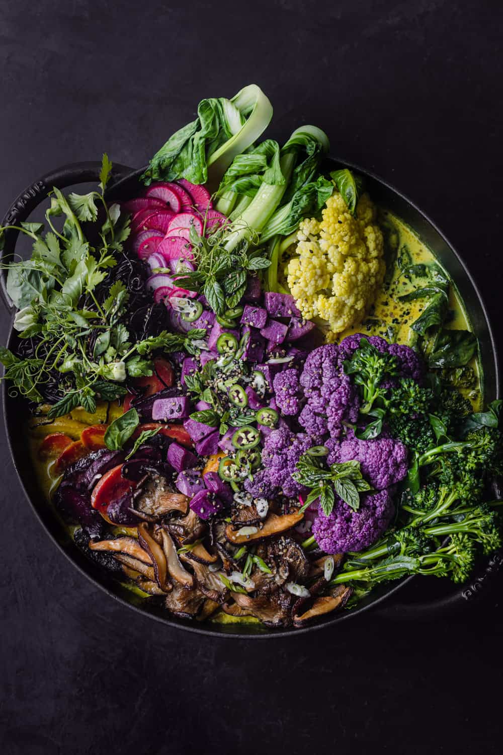 Black cast iron skillet filled with a very colorful turmeric curry noodle soup loaded with vibrant vegetables, overhead shot.