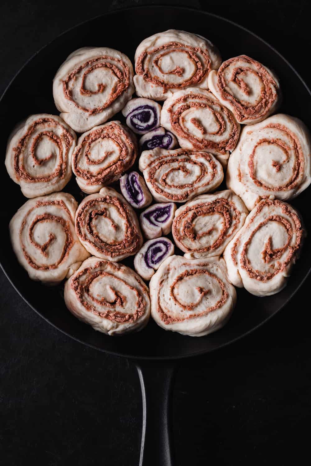 Challah Cinnamon Rolls rising in a cast iron skillet; overhead shot on a black background.