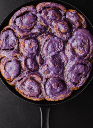 Challah Dough cinnamon rolls with an ube cream cheese frosting all done and ready to be eaten! Overhead shot on a black background.