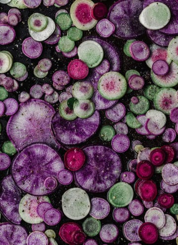 Pink, purple and green radishes thinly sliced into rounds on a baking sheet; overhead shot.