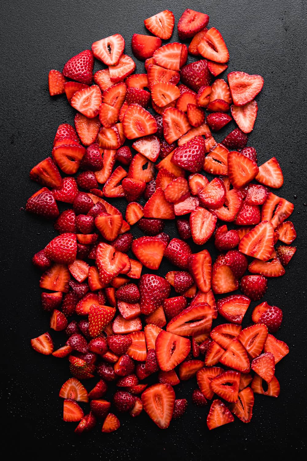 sliced strawberries on a black cutting board; overhead shot.