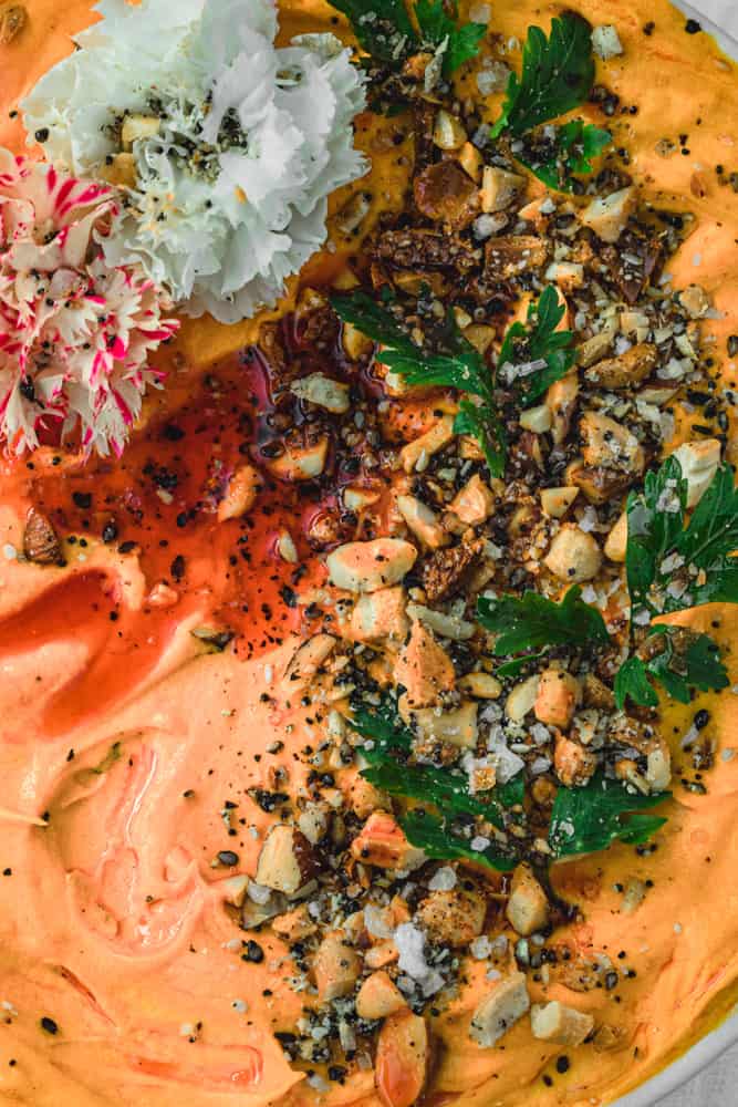 Orange carrot hummus topped with nuts, seeds, olive oil, edible flowers and spices; overhead and close up shot.